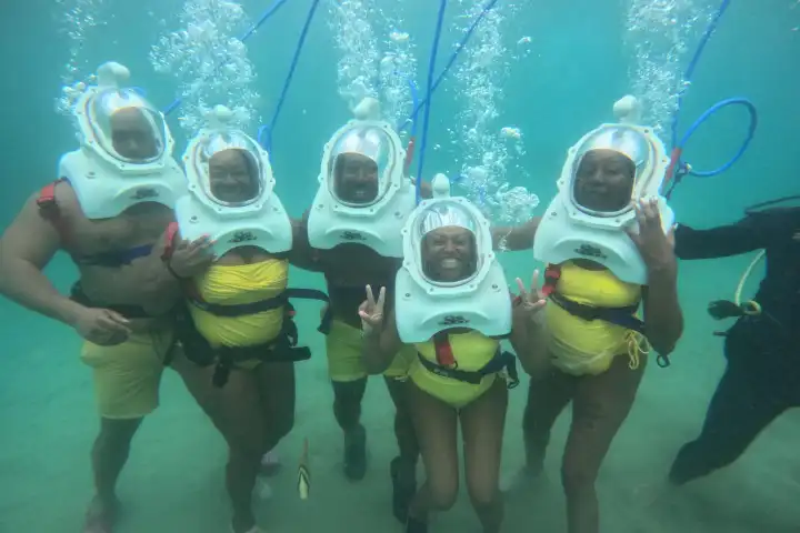 Group underwater with helmets, wearing yellow shorts, giving peace signs.